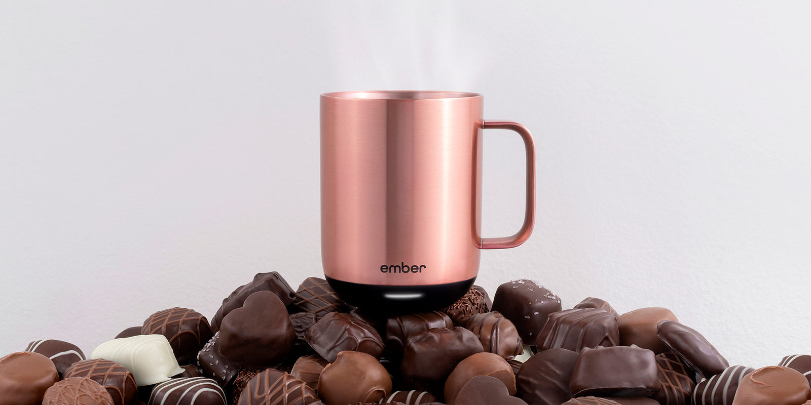 Ember Mug² in Rose Gold sitting on a pile of assorted chocolates.