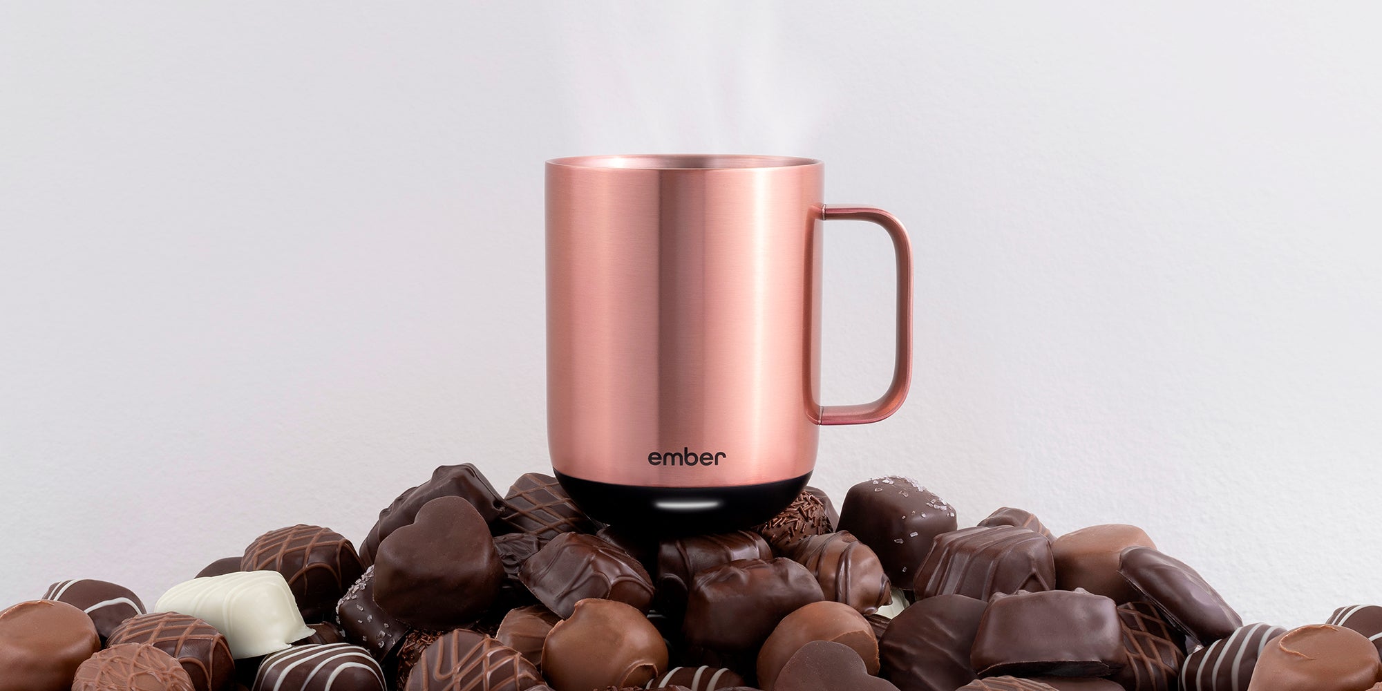 Ember Mug² in Rose Gold sitting on a pile of assorted chocolates.