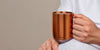 Close up of a man wearing sweatpants and holding an Ember Mug 2: Copper Edition in 14 oz with steaming coffee inside.